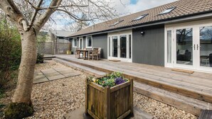 A modern house with a patio, a wooden deck, and a garden bed with flowers. - Stunning private villa for 10 guests with WIFI, TV, patio and pets allowed (Inverness)