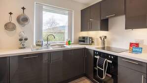 A modern kitchen with dark cabinets, a built-in oven, a microwave, and a window with a view of greenery. - Stunning private villa for 10 guests with WIFI, TV, patio and pets allowed (Inverness)