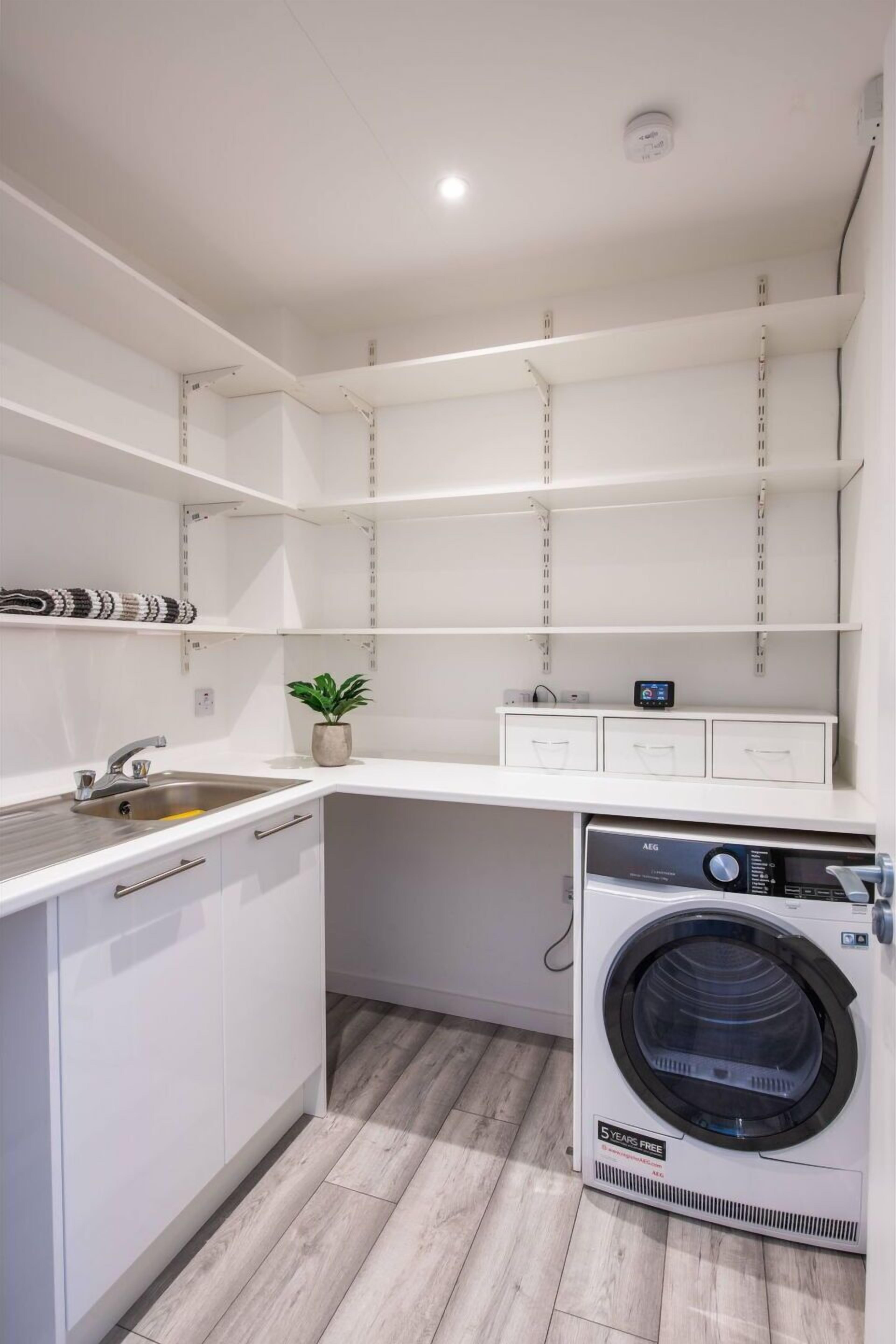 A modern laundry room with a built-in washer and dryer, a sink, and storage shelves.