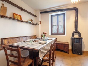 Un comedor con mantel a cuadros, sillas de madera, un banco, una ventana con cortinas y una estufa negra.
