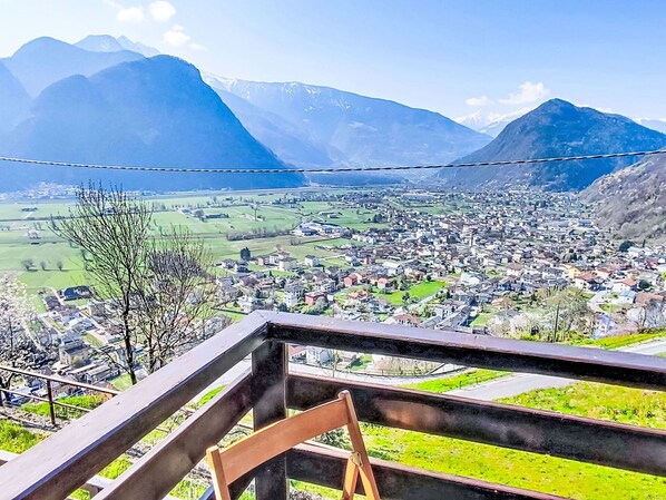 Un pueblo con montañas al fondo, cielo despejado y una baranda de madera al frente.