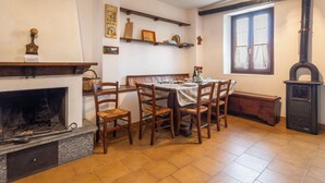 Un comedor con chimenea, sillas de madera, una mesa preparada para cuatro personas y un ventanal con cortinas.
