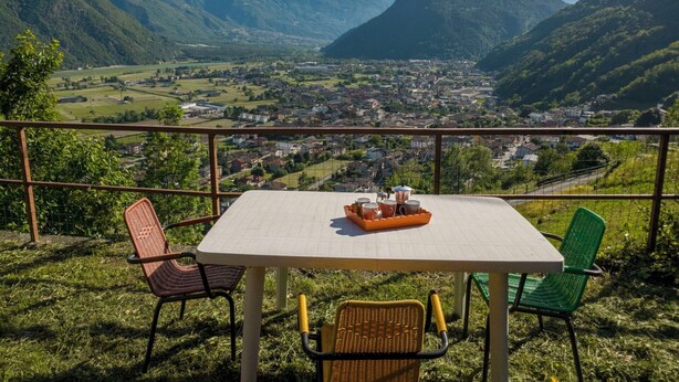 Una mesa con sillas y una bandeja de tazas, con vistas a un valle con casas y montañas.