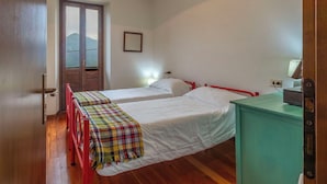 Habitación con dos camas, una puerta de madera, un ventanal con vistas a la montaña y un escritorio pequeño con lámpara.