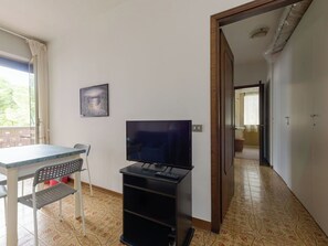 Una habitación con una televisión sobre un mueble bajo, una mesa con una silla, un suelo estampado y una puerta que da a otra habitación.