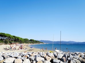 A beach with rocky foreground, people sunbathing, and boats in the water. - Nice apartment for 5 guests with WIFI, TV, terrace and pets allowed (Follonica)