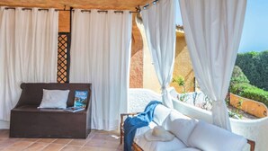Ein überdachter Außenbereich mit einer Couch und einem Sessel, einer Zeitschrift auf der Couch sowie Blick auf die Landschaft.