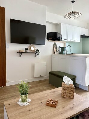 Una cocina moderna con armarios blancos, un televisor negro y una mesa de comedor de madera con una planta verde y una caja de pañuelos.