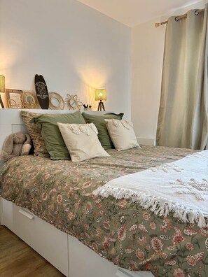 A bedroom with a bed, pillows, a teddy bear, wall decor, and a lamp.