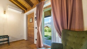 A room with wooden flooring, a green upholstered chair, a wooden door, and a view of a garden through a glass door.