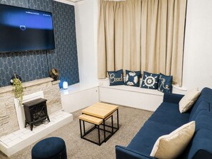 A living room with a flat-screen TV mounted on the wall, a fireplace, a blue sofa, a wooden coffee table, and decorative pillows. - The Skegness Stag & Hen House (Skegness)