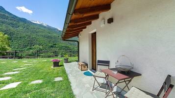 Un patio con mesa y sillas, una pérgola de madera, suelo de piedra y vistas a la montaña.