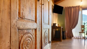 A rustic wooden cabinet with a spiral design, a television mounted on the wall, and a chair in a room with wooden flooring. - Le Rêve Guest Room - Zaya (Saint-Vincent)