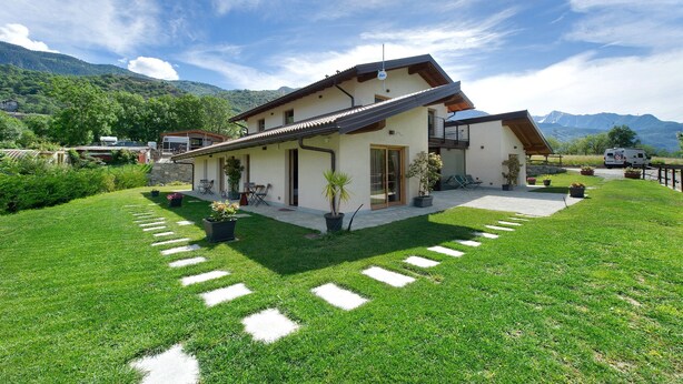 A modern house with a sloped roof, a patio with outdoor furniture, and a well-maintained lawn with stepping stones. - Le Rêve Guest Room - Zaya (Saint-Vincent)