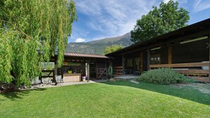 A building with a covered outdoor seating area, a grassy lawn, and a mountain backdrop. - Le Rêve Guest Room - Zaya (Saint-Vincent)