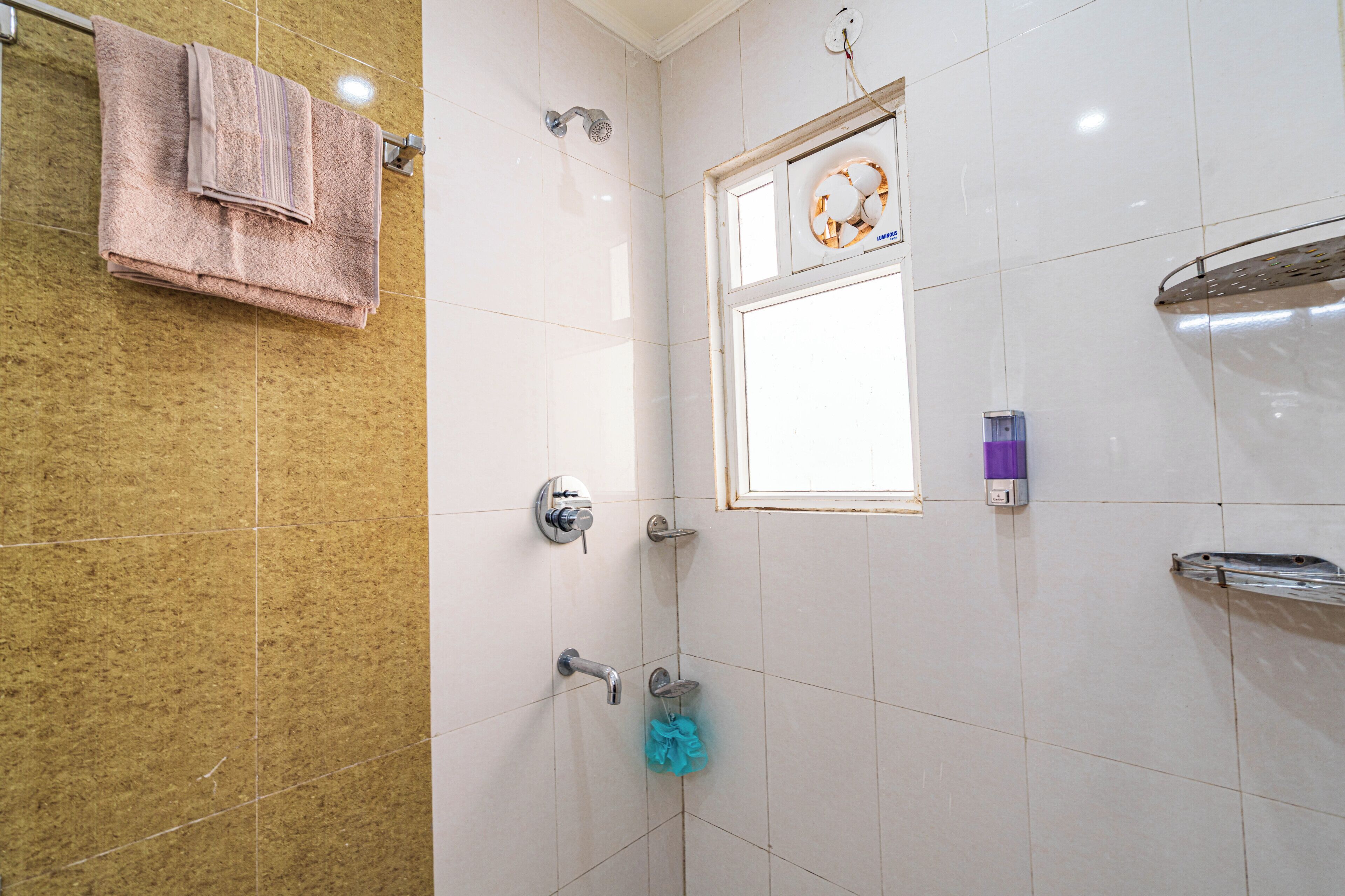 A bathroom with a shower, a towel rack, a window, and a hand dryer.