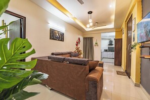 A modern living room with a sofa, a television, and a kitchen in the background. - Santa Fe 1BHK CityView by Homeyhuts (Dehradun)