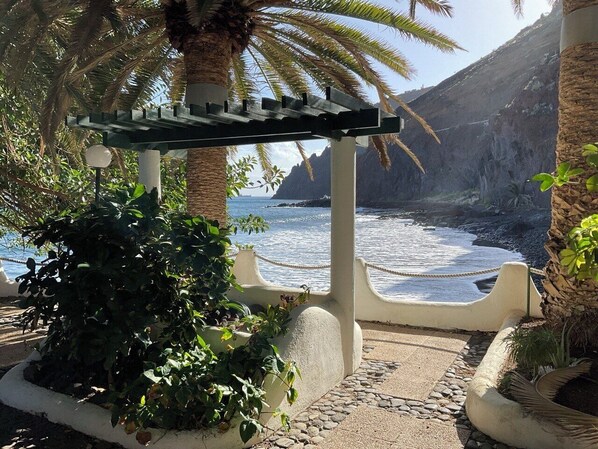 A coastal walkway with a pergola, plants, and a view of the sea and cliffs. - Oceanfront Playa Las Gaviotas – Private Beach Tenerife, Ocean Front Canarias 2 (Santa Cruz de Tenerife)