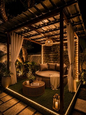 Un área de estar al aire libre con una mesa redonda, cojines y una estructura de pérgola.