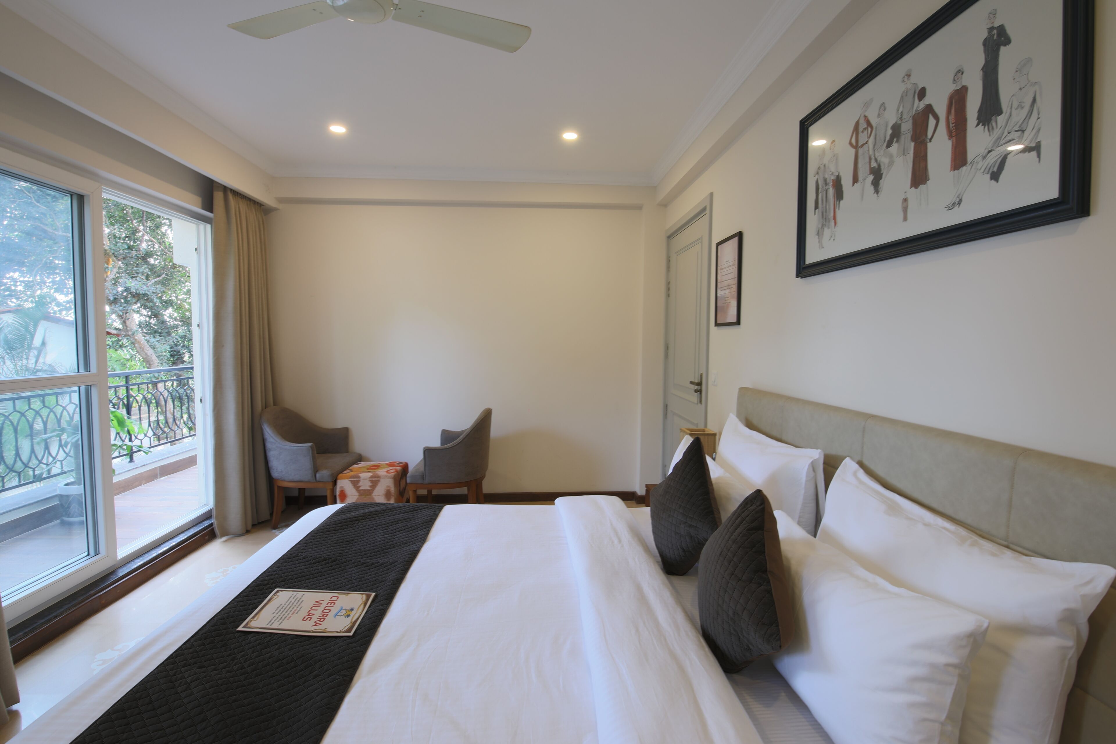 A hotel room with a bed, a chair, a small table, a window with curtains, and a ceiling fan.