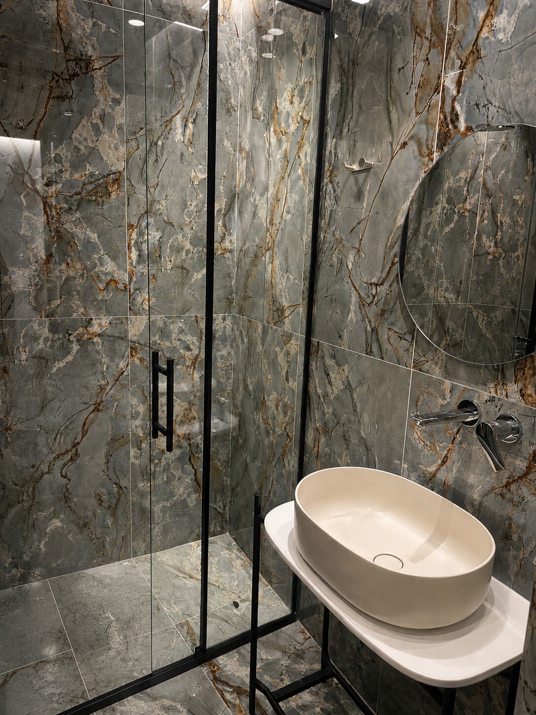 A bathroom with a glass-enclosed shower, a white sink, and a marble backsplash.