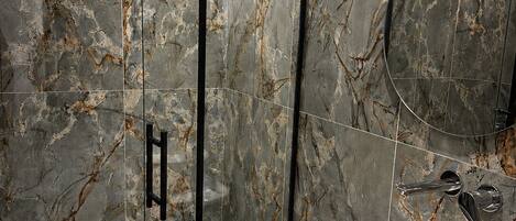 A bathroom with a glass-enclosed shower, a white sink, and a marble backsplash.