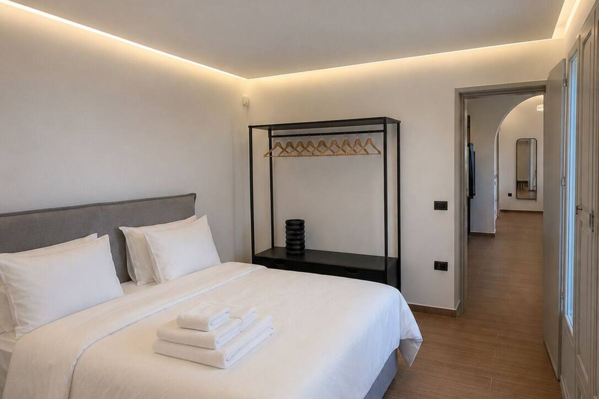 Ein modernes Hotelzimmer mit einem großen Bett, einem Nachttisch, einem Kleiderhaken und Blick in die Hotellobby.