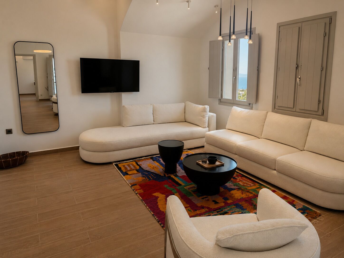 A modern living room with a sectional sofa, a flat-screen TV, a coffee table, and a colorful rug.