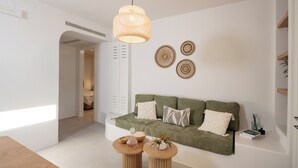 Ett modernt vardagsrum med en grön soffa, två träbord och en hängande lampa.