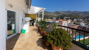 Un balcone con vista su una piscina e montagne, dotato di barbecue, piante in vaso e una porta con finestra.