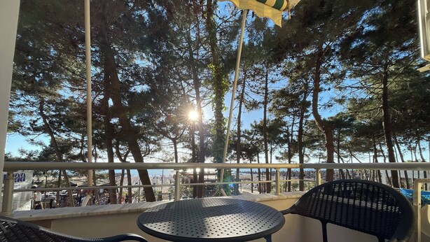 Eine Terrasse mit einem runden Tisch und zwei Stühlen mit Blick auf einen Strand und Bäume.