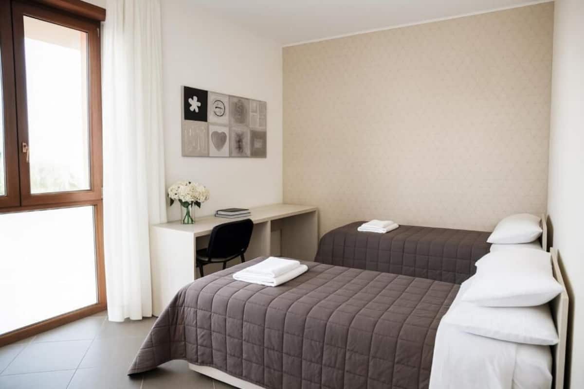 A hotel room with two beds, a desk, and a window.