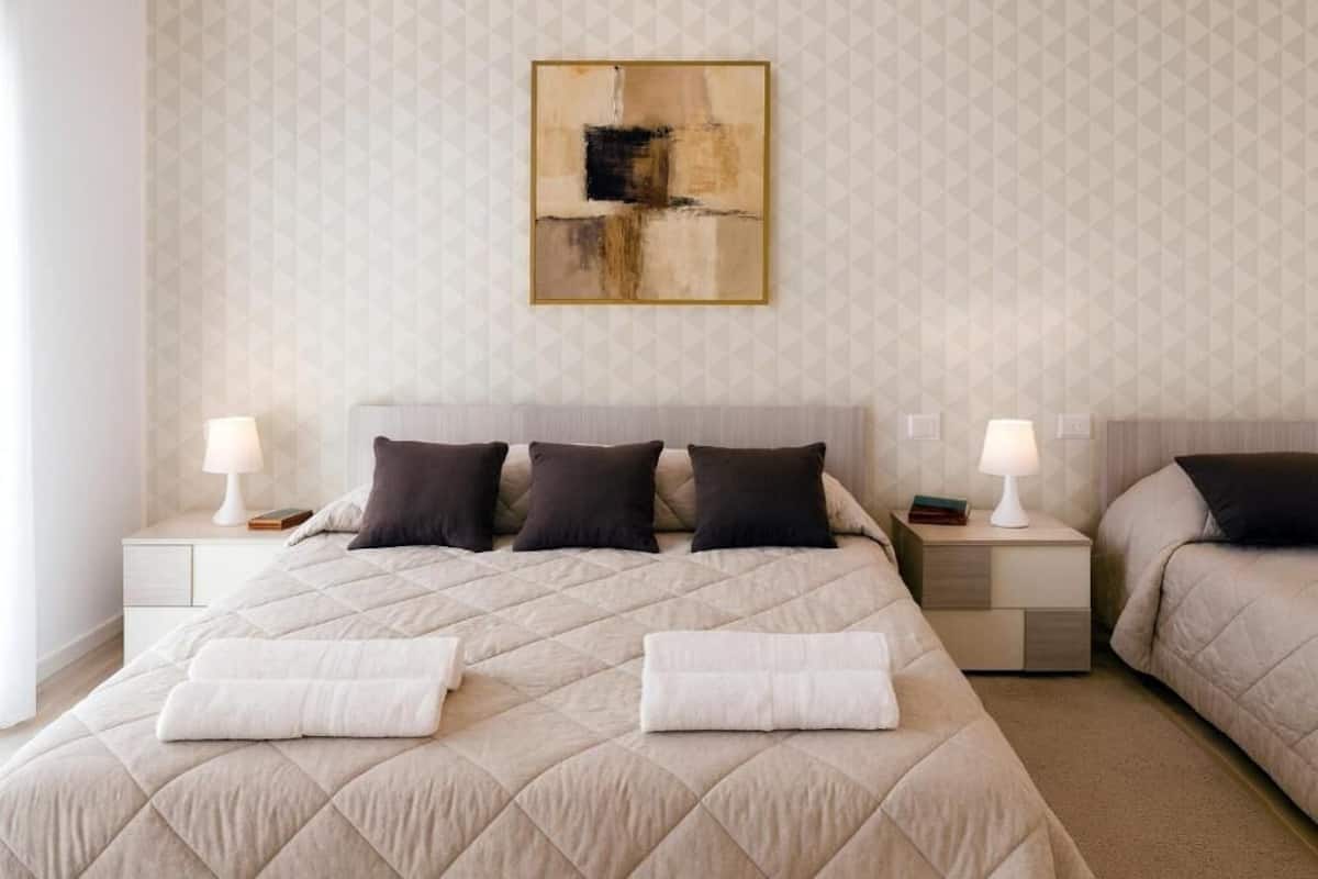 A hotel room with a large bed, two bedside tables with lamps, a geometric patterned wall, and a piece of abstract art.