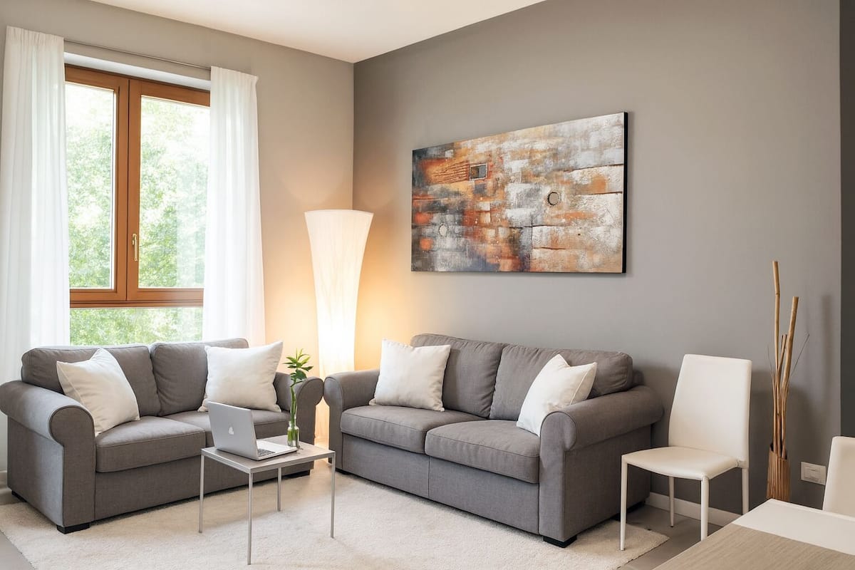 A modern living room with two grey sofas, a white coffee table, a laptop, and a large abstract painting on the wall.