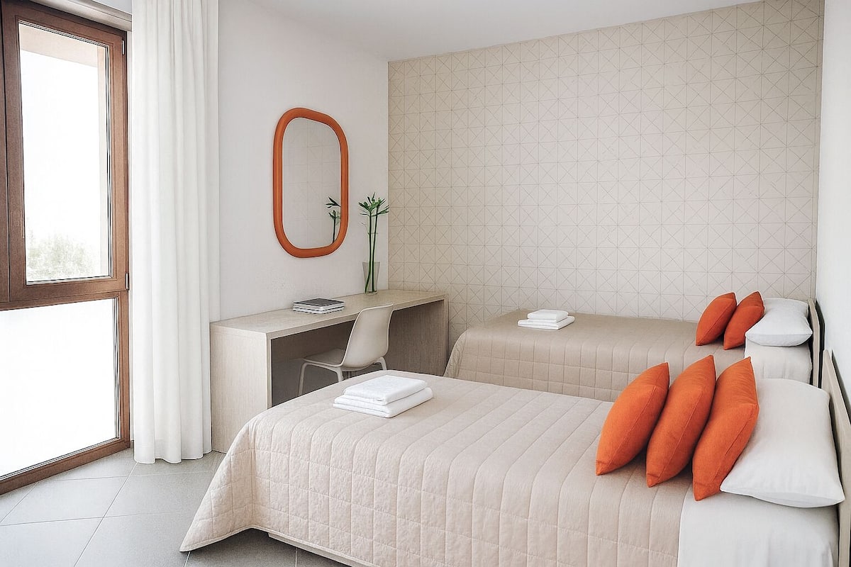 A hotel room with two beds, a desk, a mirror, and a window.