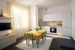 A modern kitchen with white cabinets, a dining area with a yellow table and chairs, and a flat-screen TV on a cabinet.