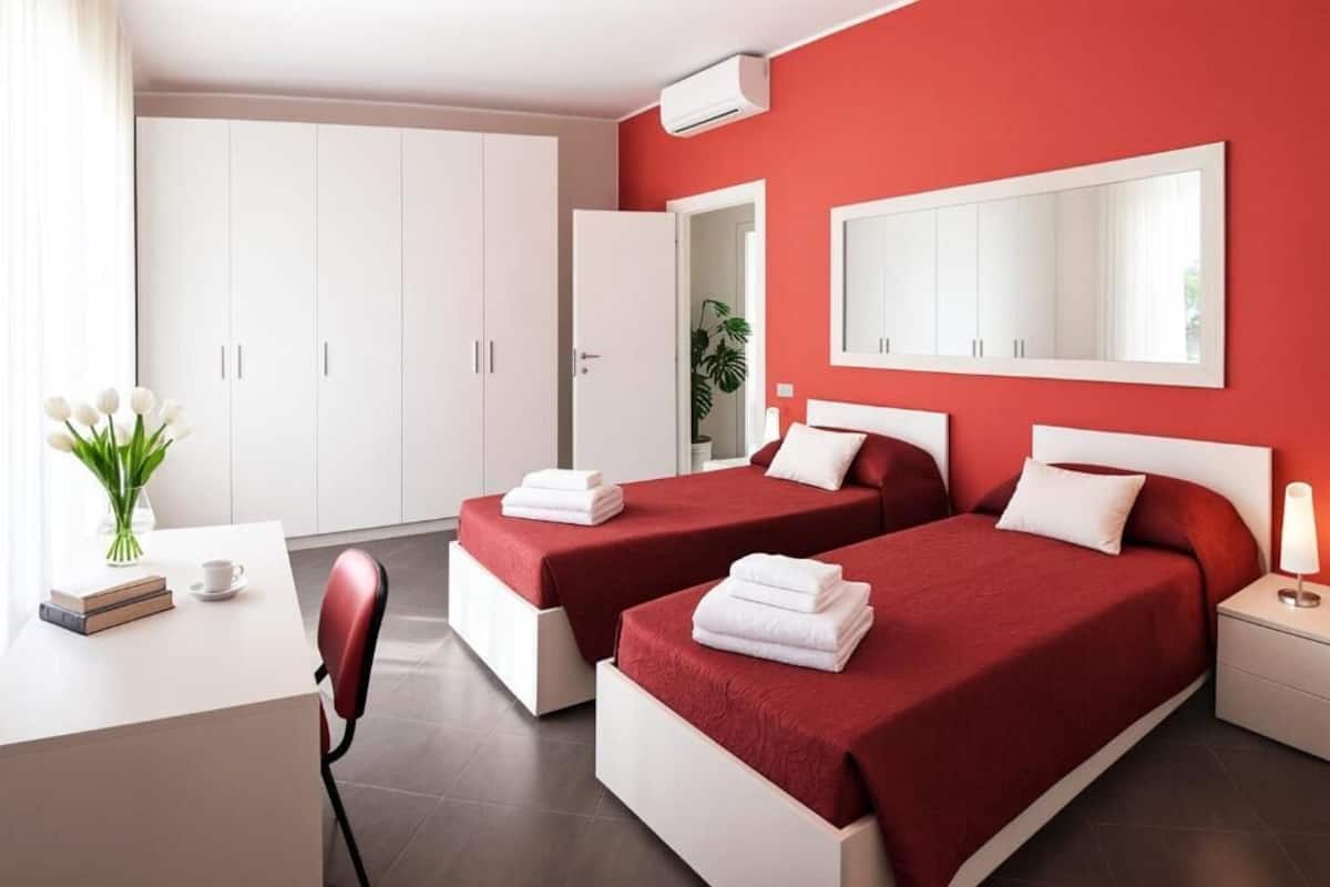 A hotel room with two beds, a desk, a chair, a mirror, and a wardrobe.