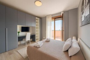 Ein Schlafzimmer mit Bett, Schreibtisch, Stuhl, Fernseher und einem Balkon.