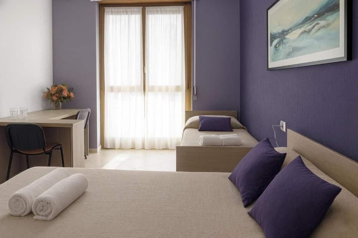 A hotel room with a bed, a desk, a chair, and a window with curtains.