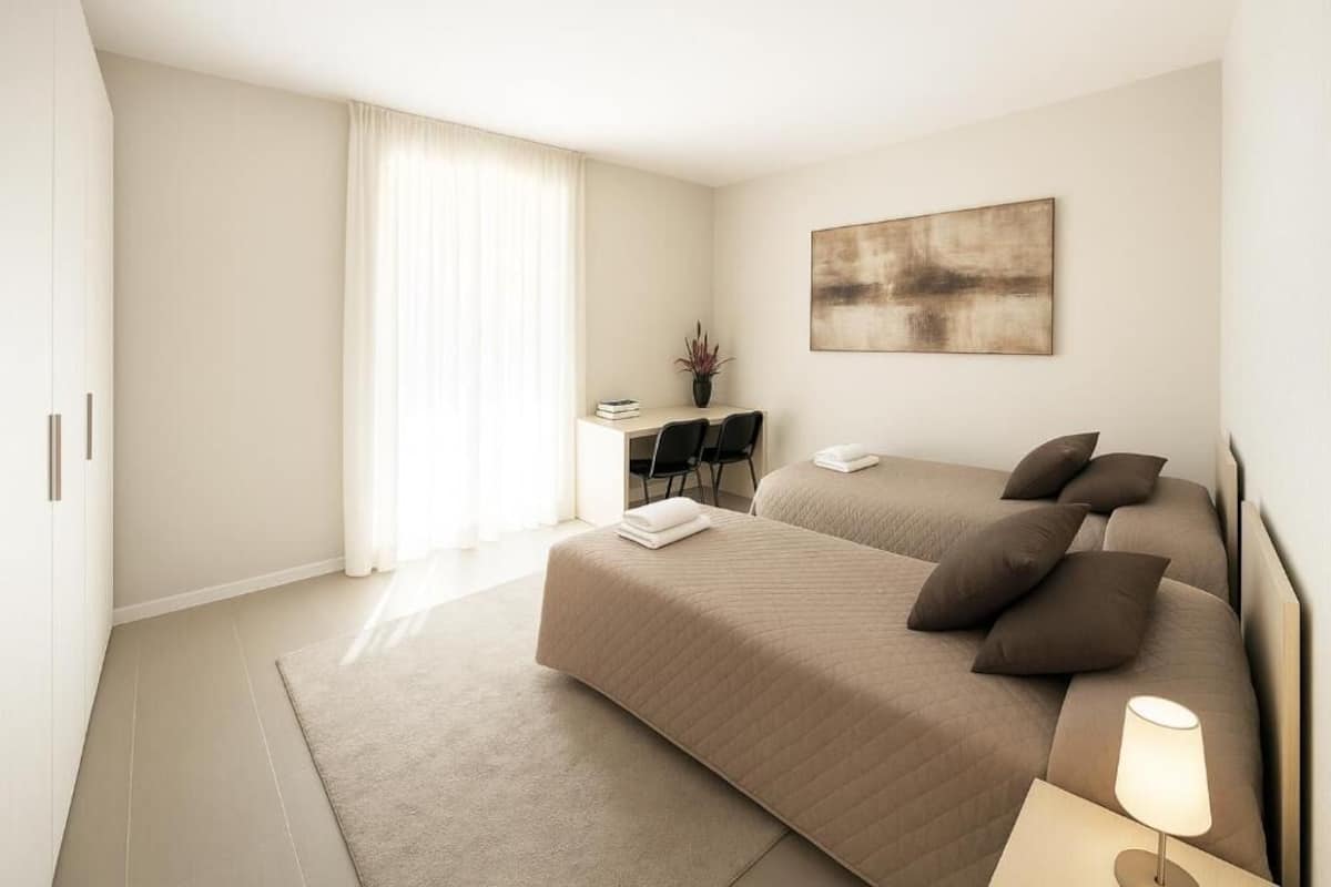 A hotel room with two beds, a desk, a chair, a lamp, and a painting on the wall.