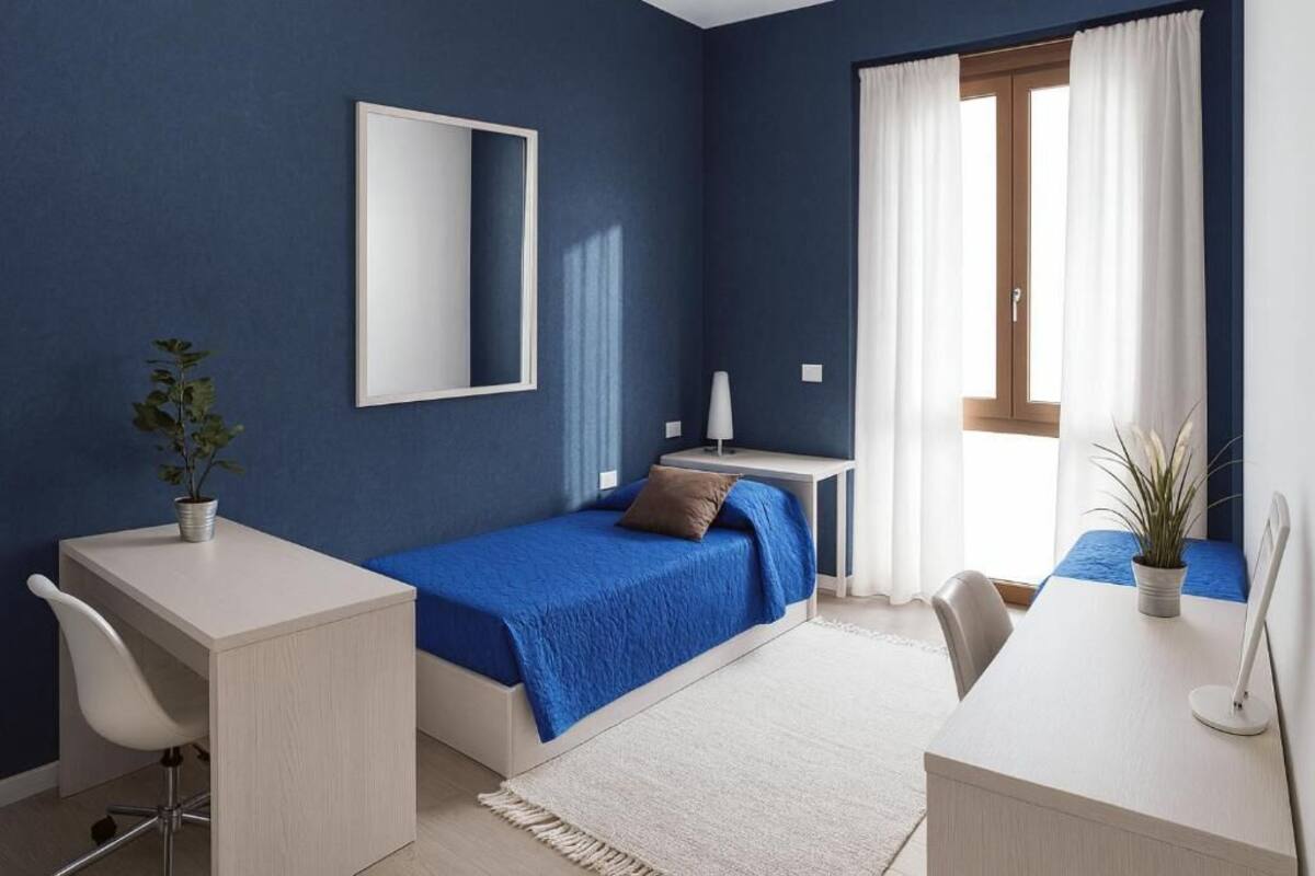A room with a bed, a desk, a chair, a mirror, and a window with curtains.