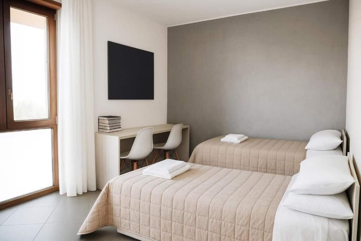 A hotel room with two beds, a desk, and a large window.
