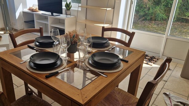 A dining table with four black plates, a glass vase with flowers, and a wooden chair.