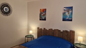 A bedroom with a wooden headboard, a blue bedspread, two bedside tables with lamps, and two posters on the wall.