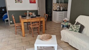 A dining area with a wooden table and chairs, a white sofa with a cushion, and a small white table with a woven basket.