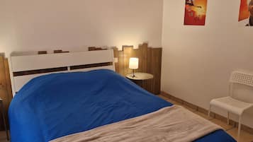 Un lit recouvert d’une couverture bleue, deux lampes de chevet, une chaise blanche et une tête de lit en bois.
