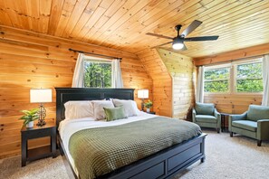 Ein Schlafzimmer mit Holzwänden, einem Bett, zwei Nachttischen, einem Deckenventilator und zwei Sesseln.