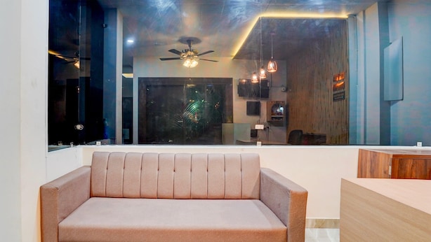 A modern living area with a sofa, a ceiling fan, pendant lights, and a view through a large window. - Super Deluxe Room Neelam Hotel (Bareilly)