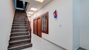 A staircase with a handrail, a fire extinguisher mounted on the wall, and a door with a window. - Super Deluxe Room Neelam Hotel (Bareilly)