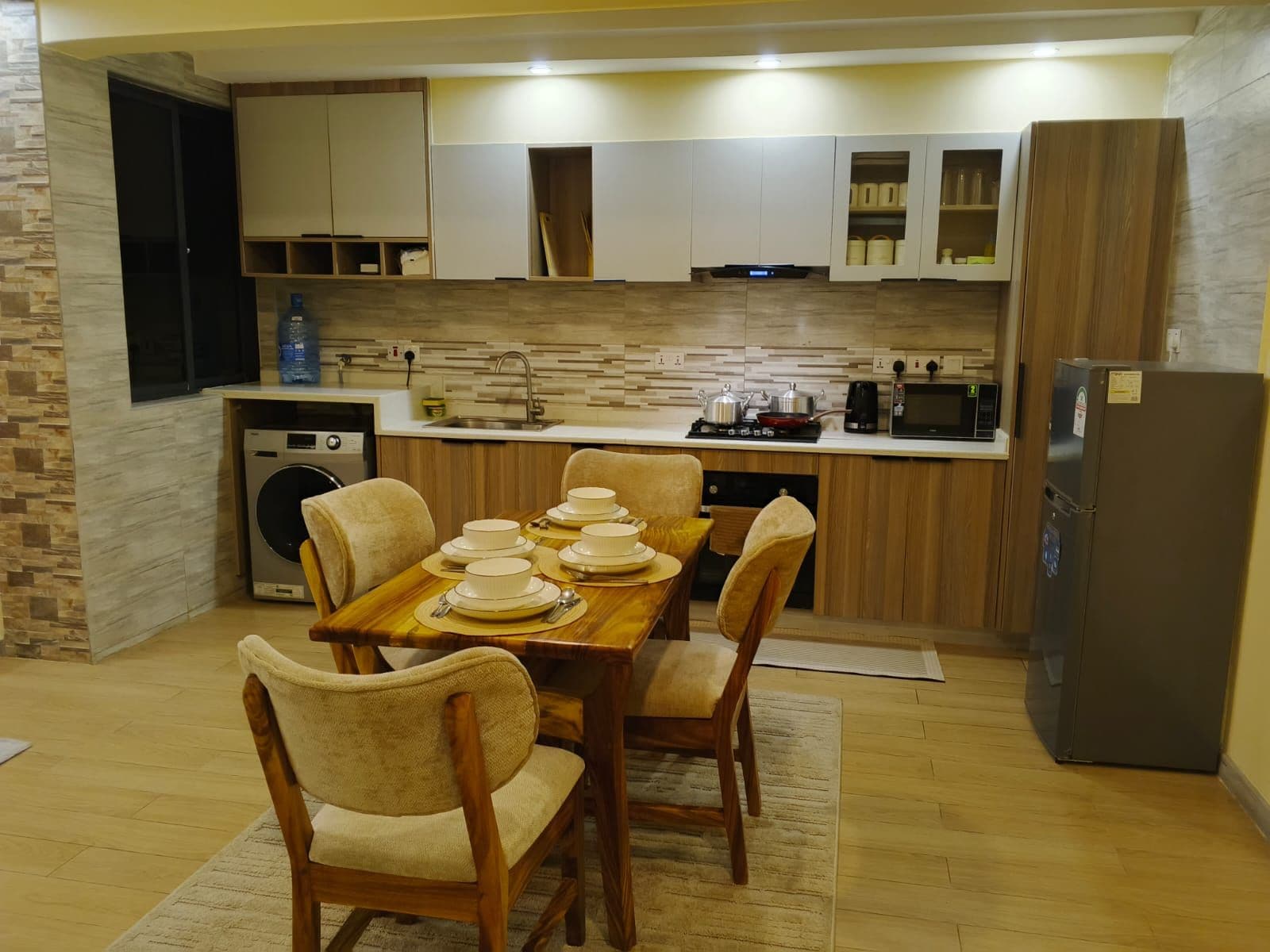 A compact kitchen with a dining table set for four, a washing machine, and a refrigerator.